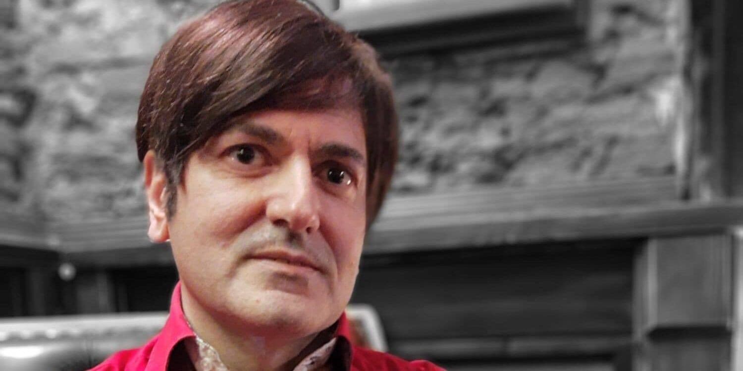 Francesco Polopoli, in camicia rossa, davanti a un muro di pietra in bianco e nero